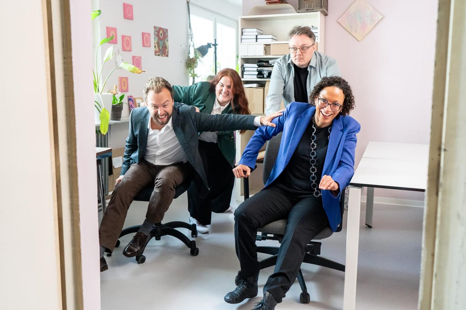 Sharon von Simson being pushed across an office in a desk chair by colleagues